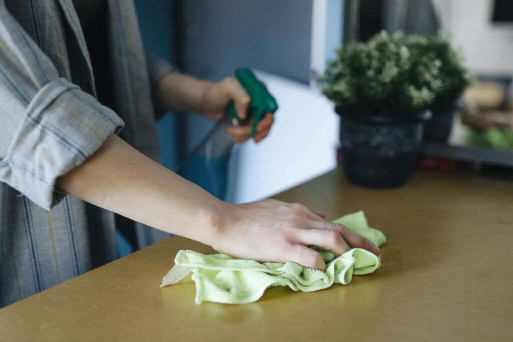 Persona limpiando una mesa con una bayeta y otra mano sosteniendo un producto limpiador Good Sense
